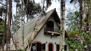 Un edificio rústico con techo de paja, rodeado de abundante vegetación y plantas en flor.