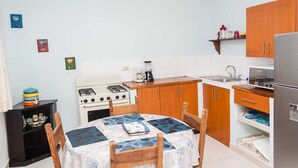 A compact kitchen with wooden cabinets, a stove, a refrigerator, and a dining table with chairs. - Studio Kin.  Close to Beaches, diving and Island Attractions. Paradise found. (Cozumel)