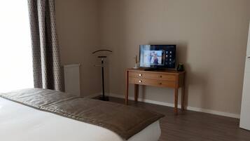 Una habitación de hotel con cama, televisor sobre un soporte de madera, lámpara de pie y radiador.
