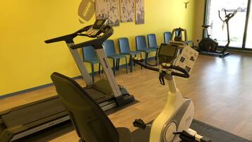 Un gimnasio con bicicletas estáticas, una cinta de correr y sillas azules.
