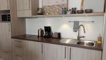 A modern kitchen with wooden cabinets, a stainless steel sink, a coffee maker, a toaster, and a microwave.