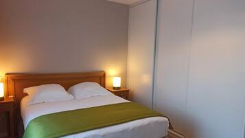 A neatly made bed with a green blanket, two bedside lamps, and a wooden headboard in a hotel room.