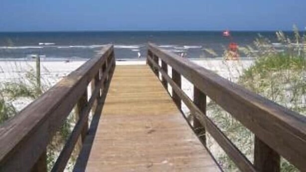 A wooden boardwalk leading to a beach with sand dunes and the ocean in the background.