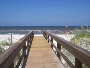 A wooden boardwalk leading to a beach with sand dunes and the ocean in the background.
