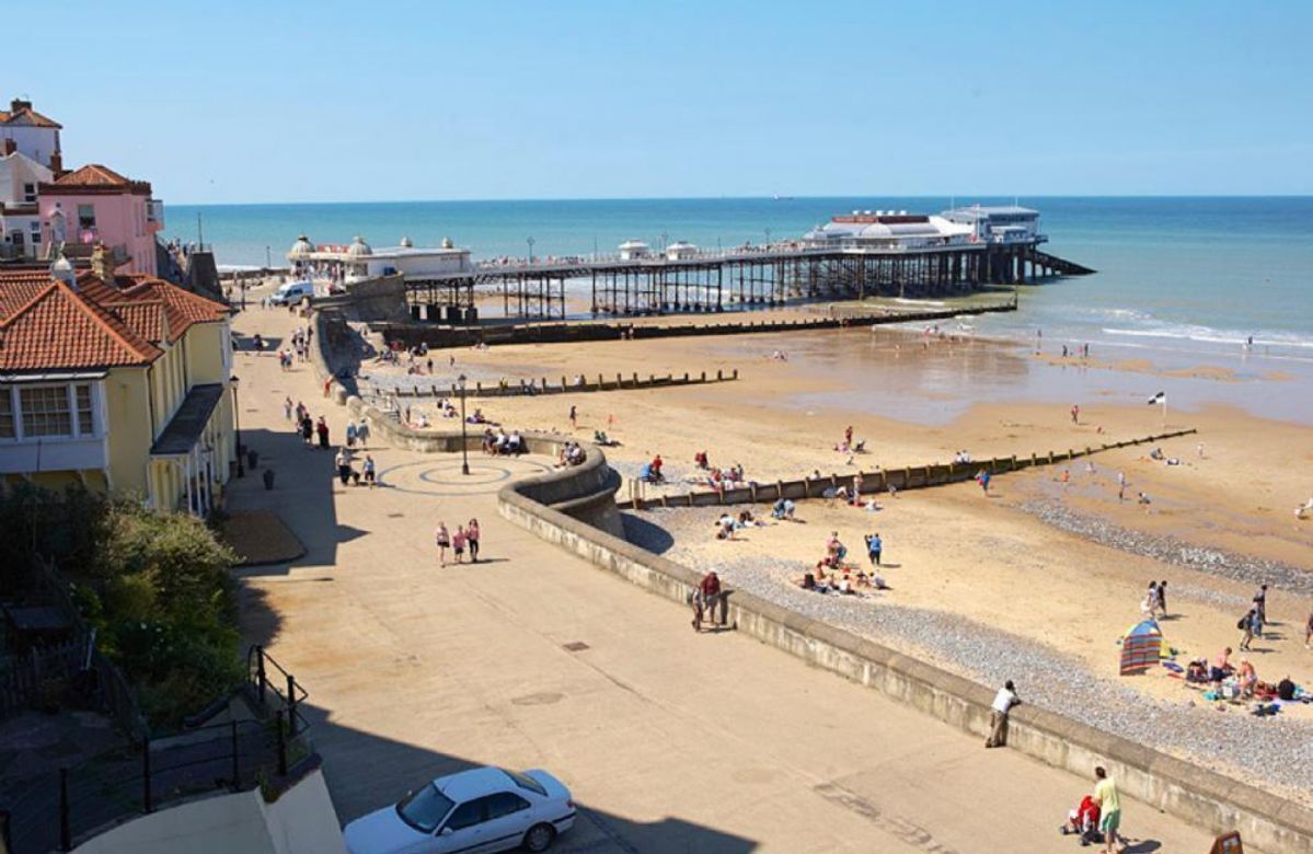 A beach with a pier, a parking area, and buildings in the background.