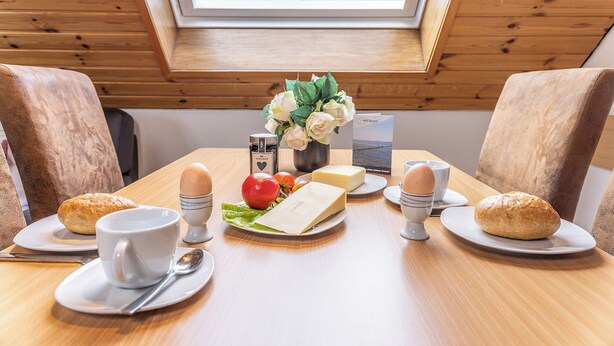 Ein Esstisch mit Frühstücksgebäck, eine Blumenvase und Blick auf ein Gebäude durch ein Oberlicht.