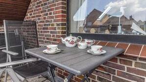 Eine Terrasse mit Tisch, der für Tee gedeckt ist, einem Stuhl und Blick auf eine Ziegelwand und ein Fenster.