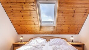 Ein Schlafzimmer mit schrägen Wänden, einem Oberlicht, zwei Nachttischlampen und einem Bett mit weißer Bettwäsche.