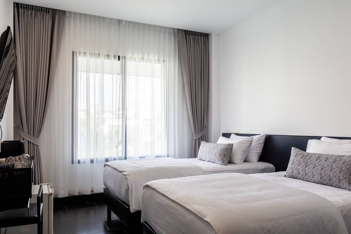 A hotel room with two beds, a desk, and a large window with curtains.
