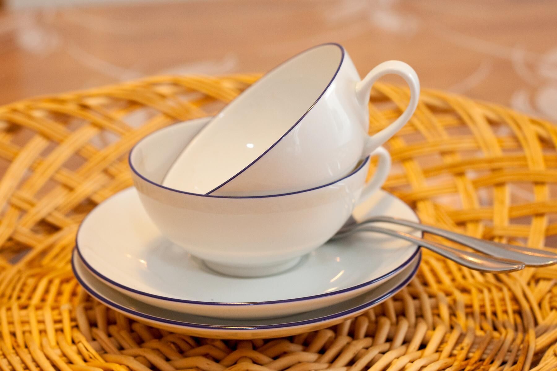 Une tasse à thé blanche, ornée d’un bord bleu, posée sur une soucoupe assortie, elle-même placée sur un tapis tissé.