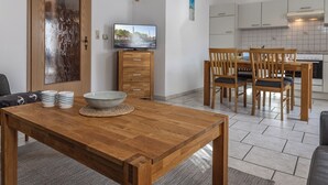 A modern kitchen with white cabinets, a wooden dining table with chairs, and a television on a wooden cabinet.