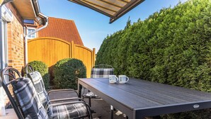 An outdoor patio with a table and chairs, a wooden fence, and a hedge.