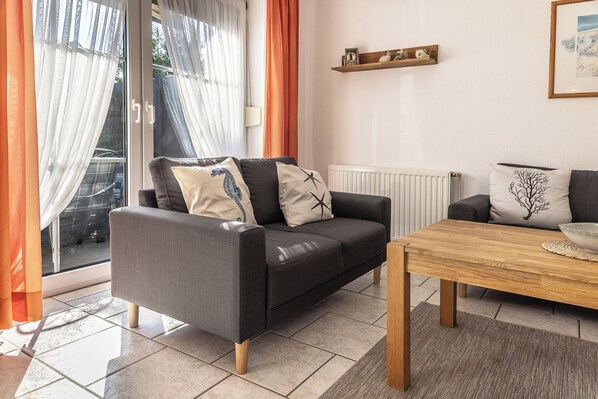 Ein modernes Wohnzimmer mit grauem Sofa, Couchtisch aus Holz und Blick durch eine Glastür.