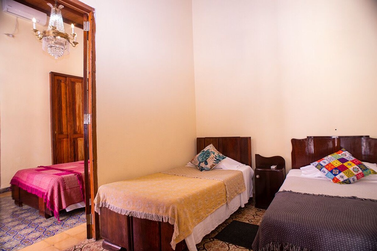 A room with two single beds, a wooden wardrobe, a chandelier, and a patterned floor.