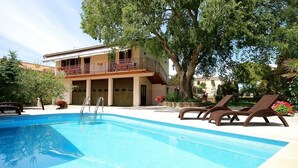 A swimming pool with lounge chairs, a building with a balcony, and a tree. - Apartment with pool and pets are also allowed (Krnica)