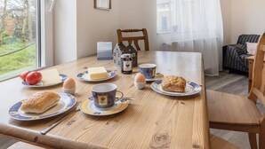 Une table de salle à manger en bois, mise pour le petit-déjeuner, avec du pain, des œufs et du beurre.