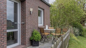 Une maison en briques avec un patio comprenant une table et des chaises, une plante en pot et une clôture en bois.
