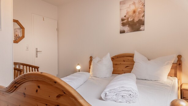 Un lit bien fait, avec du linge de lit blanc et des oreillers, une tête de lit en bois, une lampe de chevet et un tableau encadré accroché au mur.