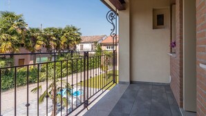 Een balkon met uitzicht op een zwembad, palmbomen en omliggende gebouwen.