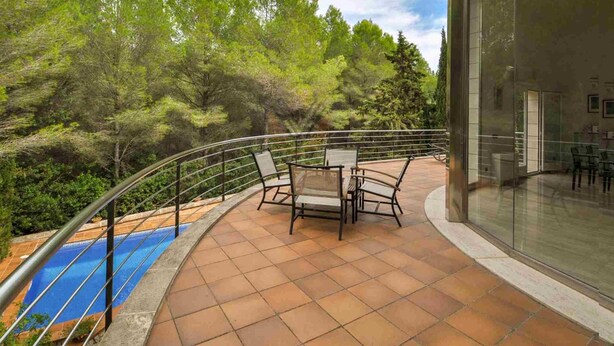 Un balcón con piscina, mobiliario exterior y vistas a árboles.