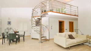 Un espacio habitable moderno con una escalera espiral central, un área de comedor con una mesa de vidrio y un sofá.