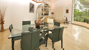 Un comedor moderno con una mesa y sillas de vidrio, una escalera de caracol y un amplio ventanal con vistas a zonas verdes.