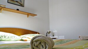 A neatly made bed with a rolled towel, a bedside lamp, and a shelf above the bed. - On the first floor with balcony and sea view (Nin)