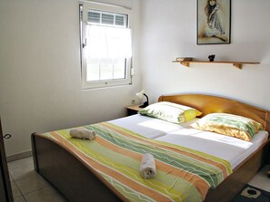 Un lit bien fait, avec une literie à rayures, une table de chevet avec une lampe, une fenêtre avec des stores et un tableau accroché au mur.