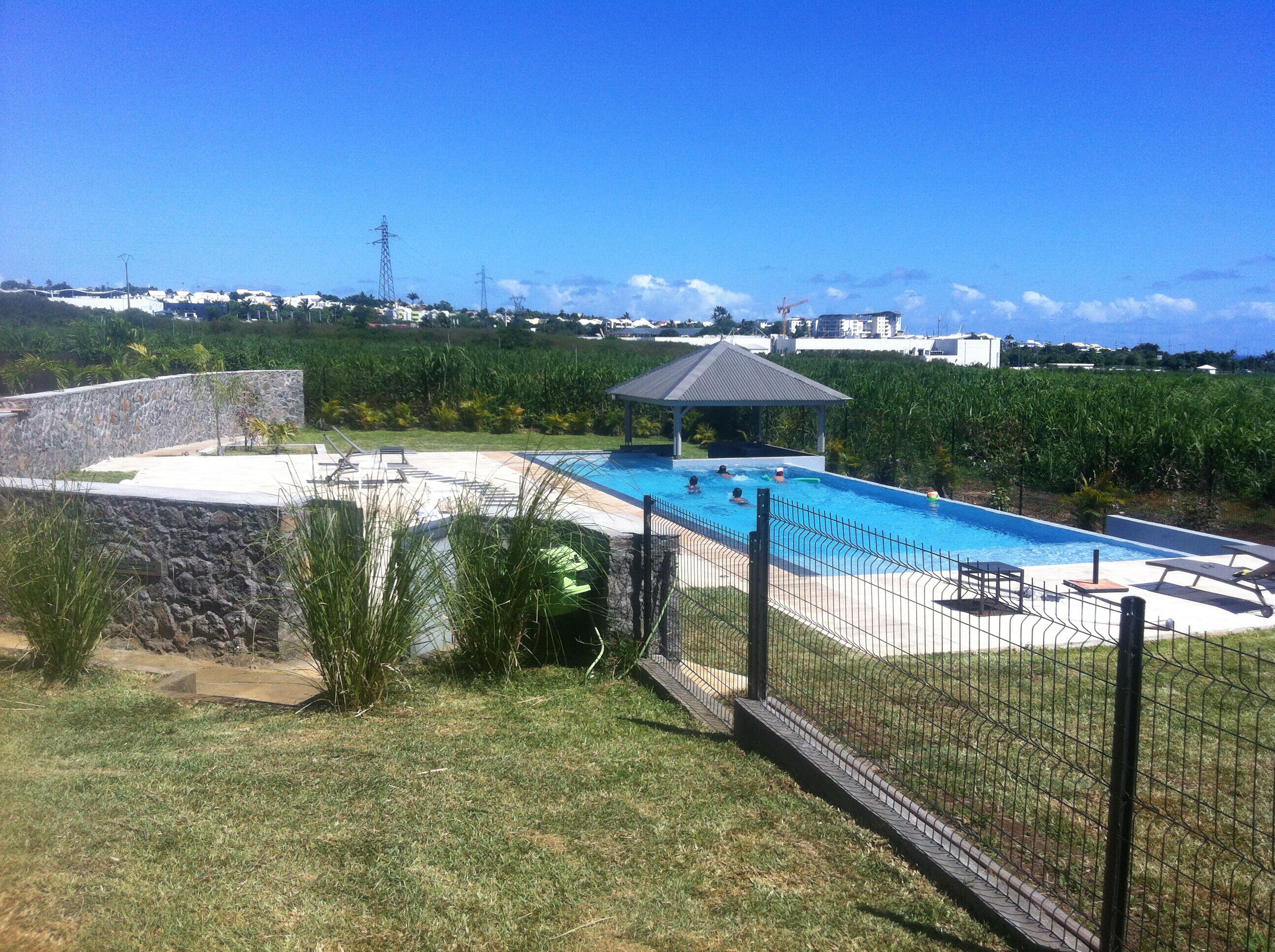 Una piscina con un pabellón, rodeada por un muro de piedra y una zona ajardinada.