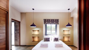 Une chambre moderne avec un grand lit, deux lampes suspendues, une fenêtre offrant une belle vue et des étagères intégrées.