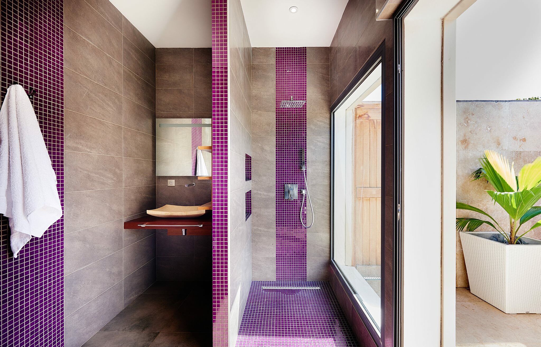 A modern bathroom with a large mirror, a wooden vanity, and a shower area with purple tiles.