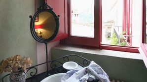 A bathroom with a white sink, a mirror, a vase with flowers, and a window with red shutters.