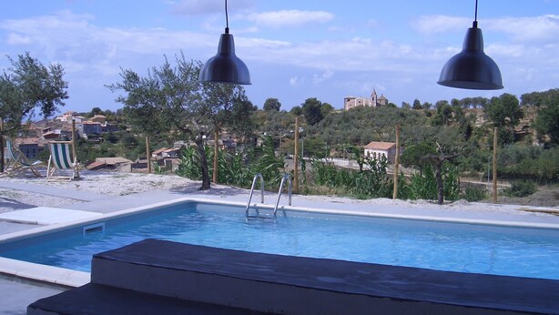 A swimming pool with a view of a hillside village, two pendant lights, and a small ladder leading into the pool.