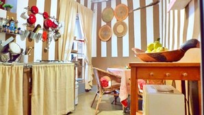A kitchen with striped wallpaper, a dining table with a bowl of fruit, and various kitchen utensils hanging on the wall.