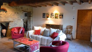 Una sala de estar acogedora con pared de piedra, vigas de madera, un conjunto de sofás, un sillón rojo, una silla de madera y una chimenea.