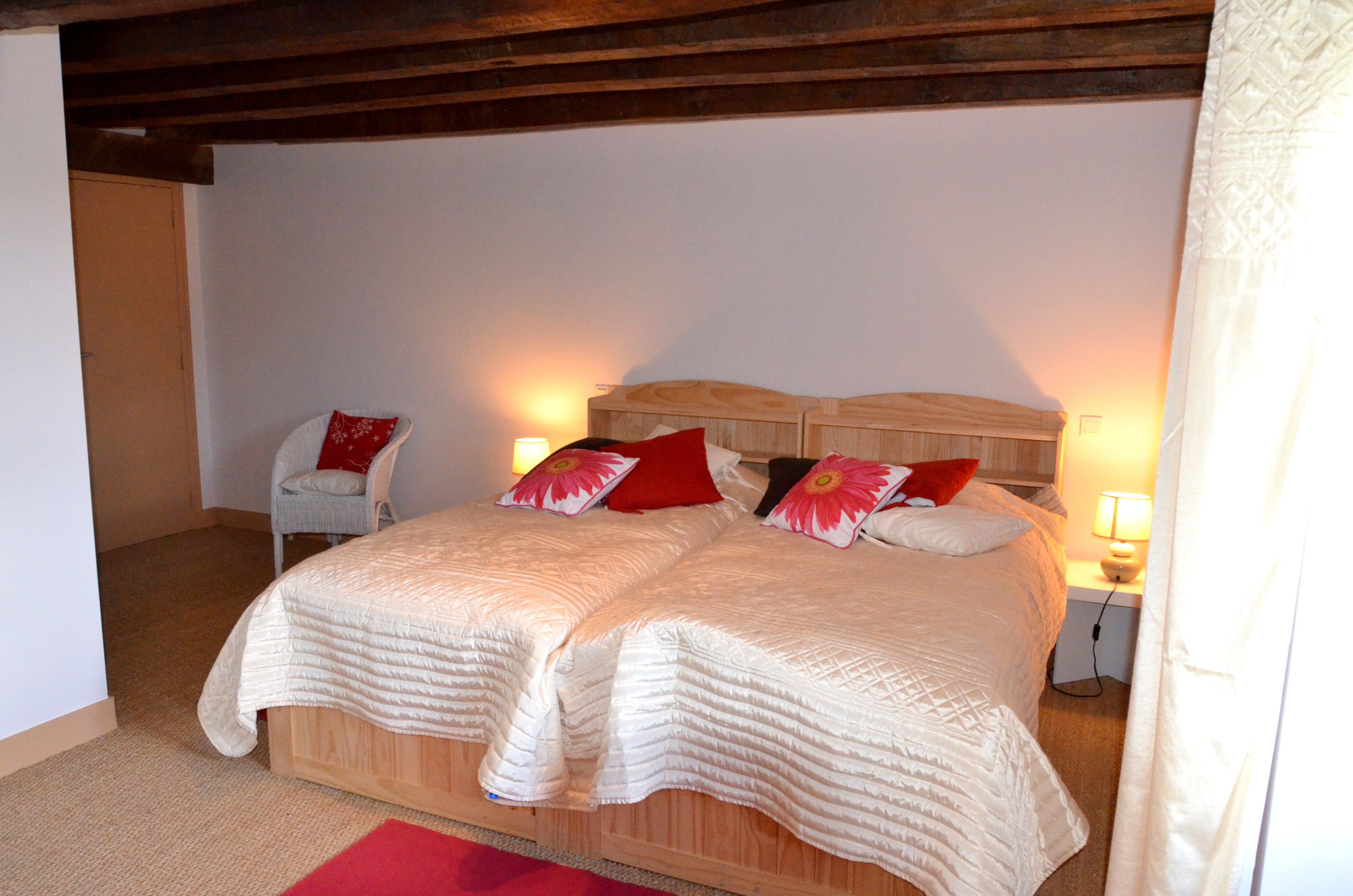 A double bed with a wooden headboard, two bedside lamps, and red and white pillows.