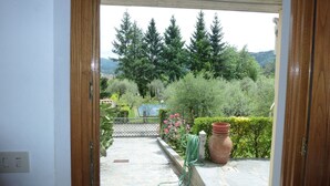 Une terrasse dallée de pierres, avec vue sur un jardin, un grand pot en terre cuite et un tuyau d’arrosage vert.