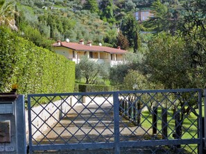 A gated entrance to a property with a paved driveway leading to a yellow building with a red roof. - Vacation apartment with private pool for 6 people. Garden, terrace, (Camaiore)