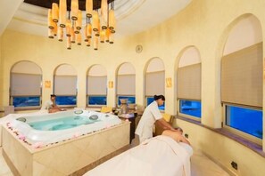 Een spa-ruimte met een groot bad, boogramen en een kroonluchter aan het plafond.