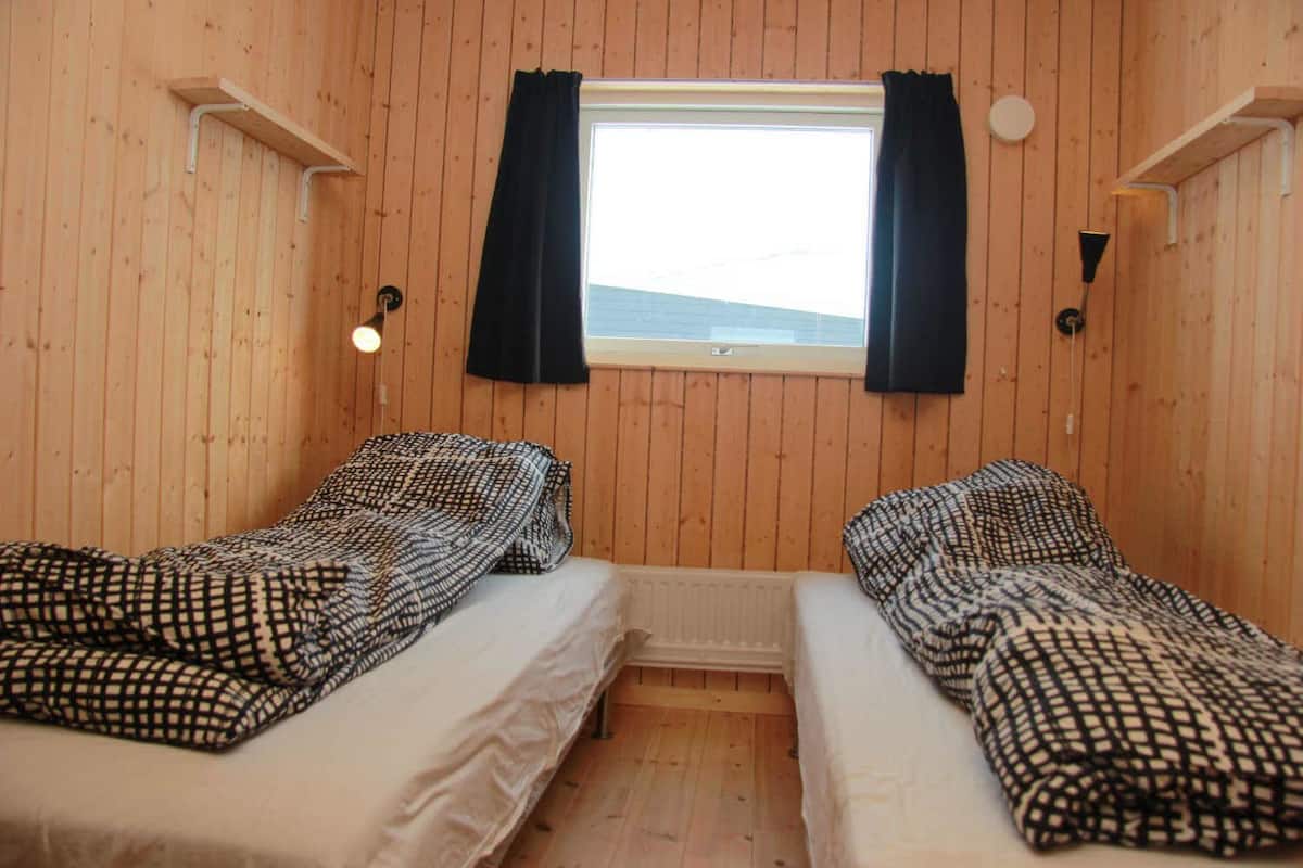 A small cabin with two beds, a window with curtains, and a wooden interior.