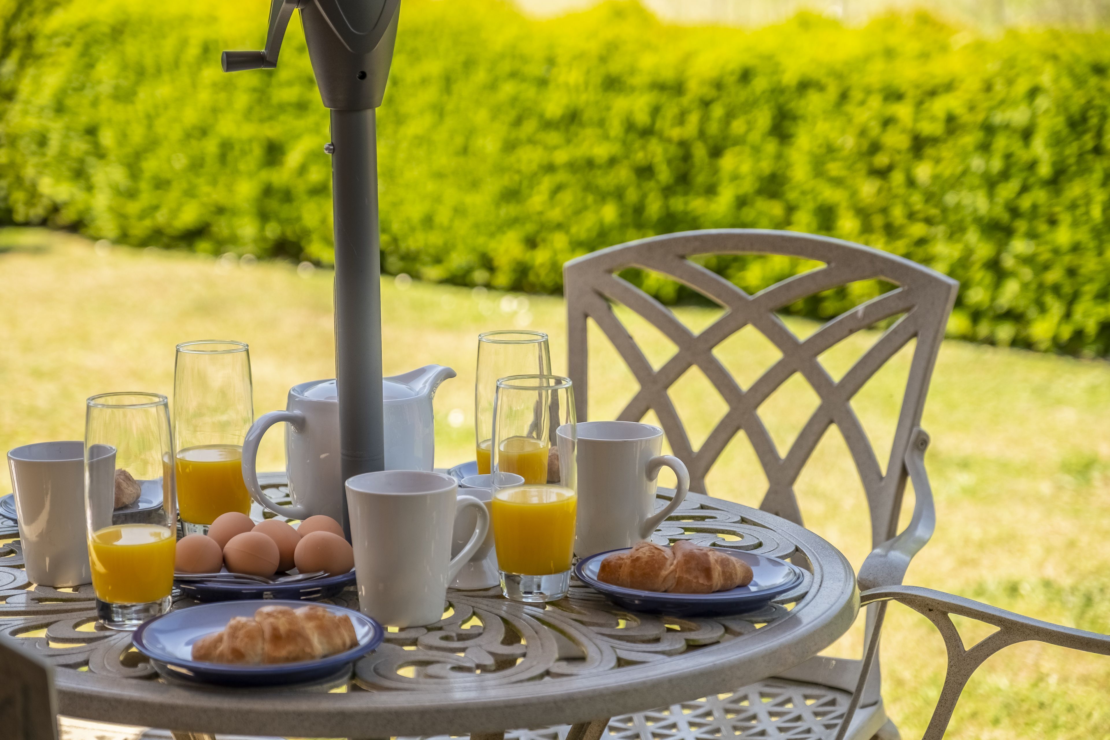 A round metal table with breakfast items including eggs, juice, and croissants.