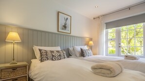 A hotel room with two beds, a large window, a framed picture on the wall, and a bedside table with a lamp.