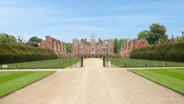 A large, symmetrical building with a central entrance, surrounded by well-manicured lawns and a gravel path leading to the entrance.
