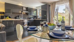 A modern kitchen with dark cabinetry, a glass dining table set with blue plates, and a view of the outdoors through large windows.