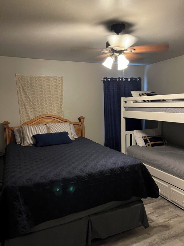 A bedroom with a single bed, a bunk bed, a ceiling fan, and a window with curtains.