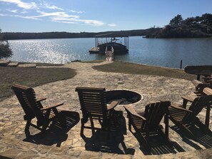 An outdoor seating area with stone flooring and wooden furniture overlooking a lake.