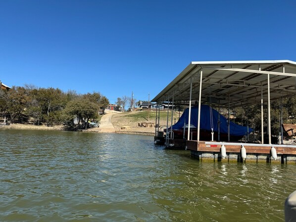 A dock with a covered boat storage area, calm water, and a clear sky.