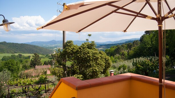A balcony with a view of a green landscape, a table, and a hanging light fixture. - Isolated and peaceful farm located on the slopes of an enchanting valley (Riparbella)