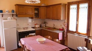 A kitchen with wooden cabinets, a white refrigerator, a stove, and a table with a checkered tablecloth. - Isolated and peaceful farm located on the slopes of an enchanting valley (Riparbella)