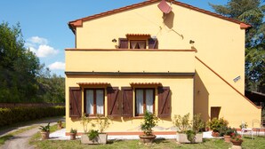 A two-story building with a yellow facade, brown shutters, and a red roof. There are potted plants in front and a satellite dish on the roof. - Isolated and peaceful farm located on the slopes of an enchanting valley (Riparbella)